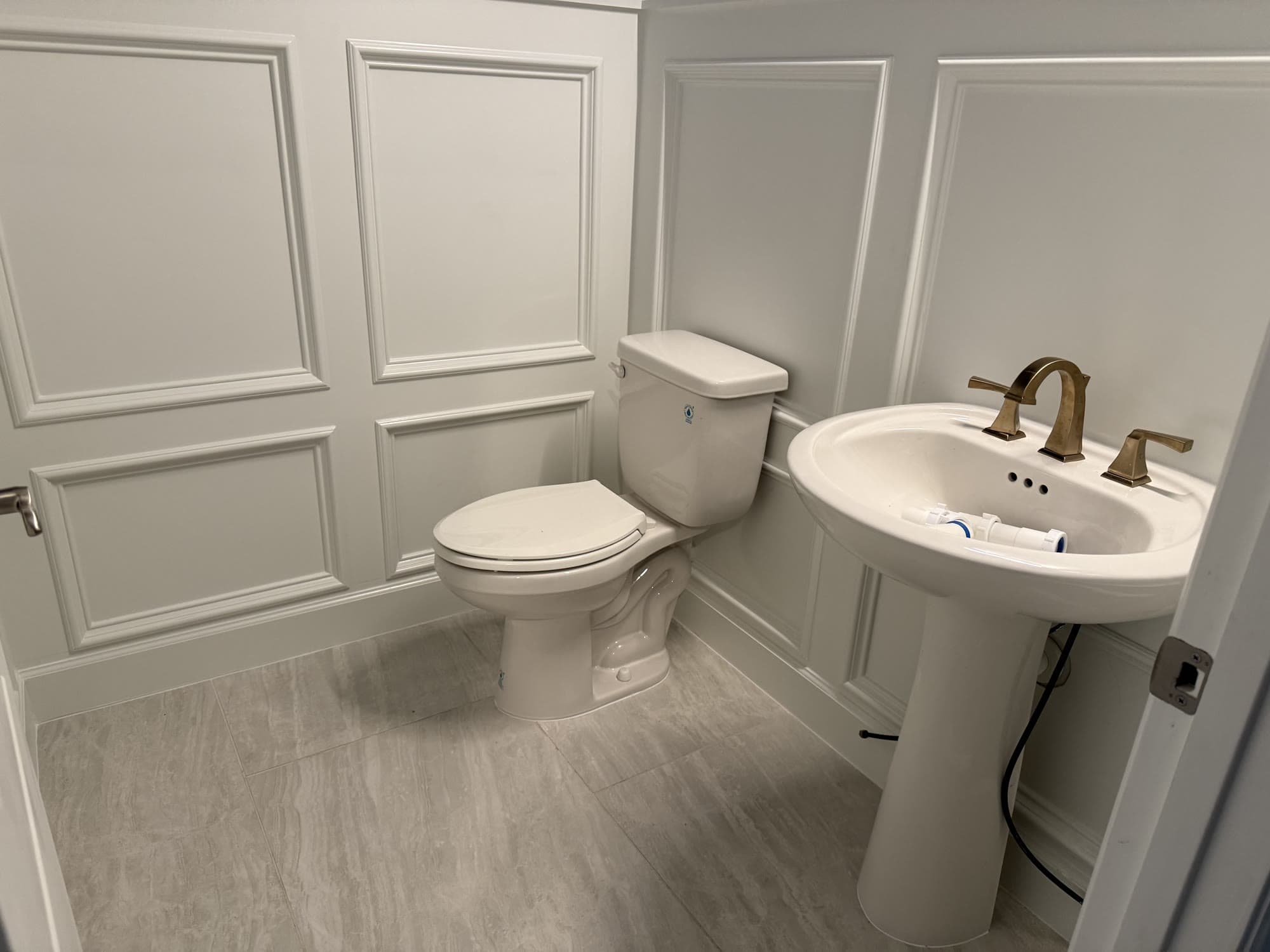 Completed powder room remodel with wainscoting, pedestal sink, and brass fixtures