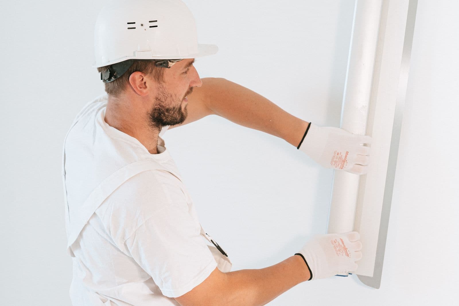 Contractor in a hard hat installing a drywall panel on an interior wall