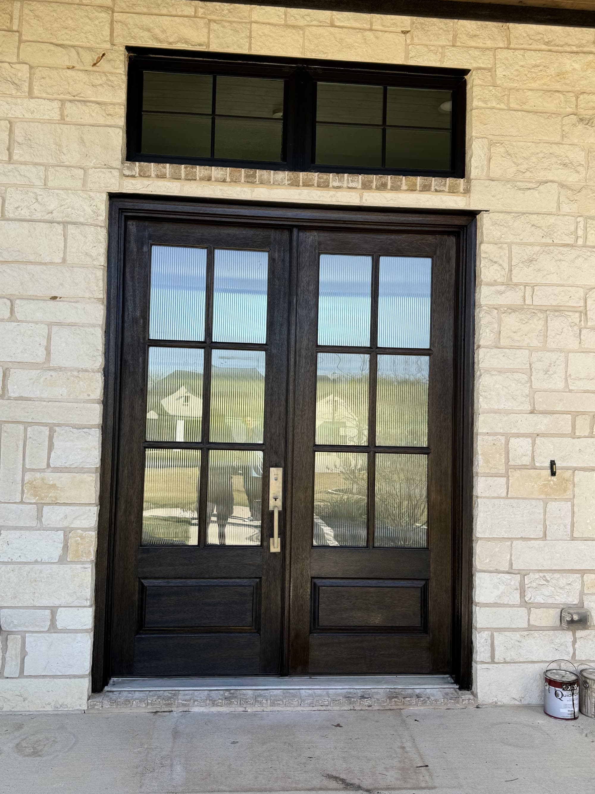 Freshly stained dark wood double entry doors on a stone home exterior after refinishing