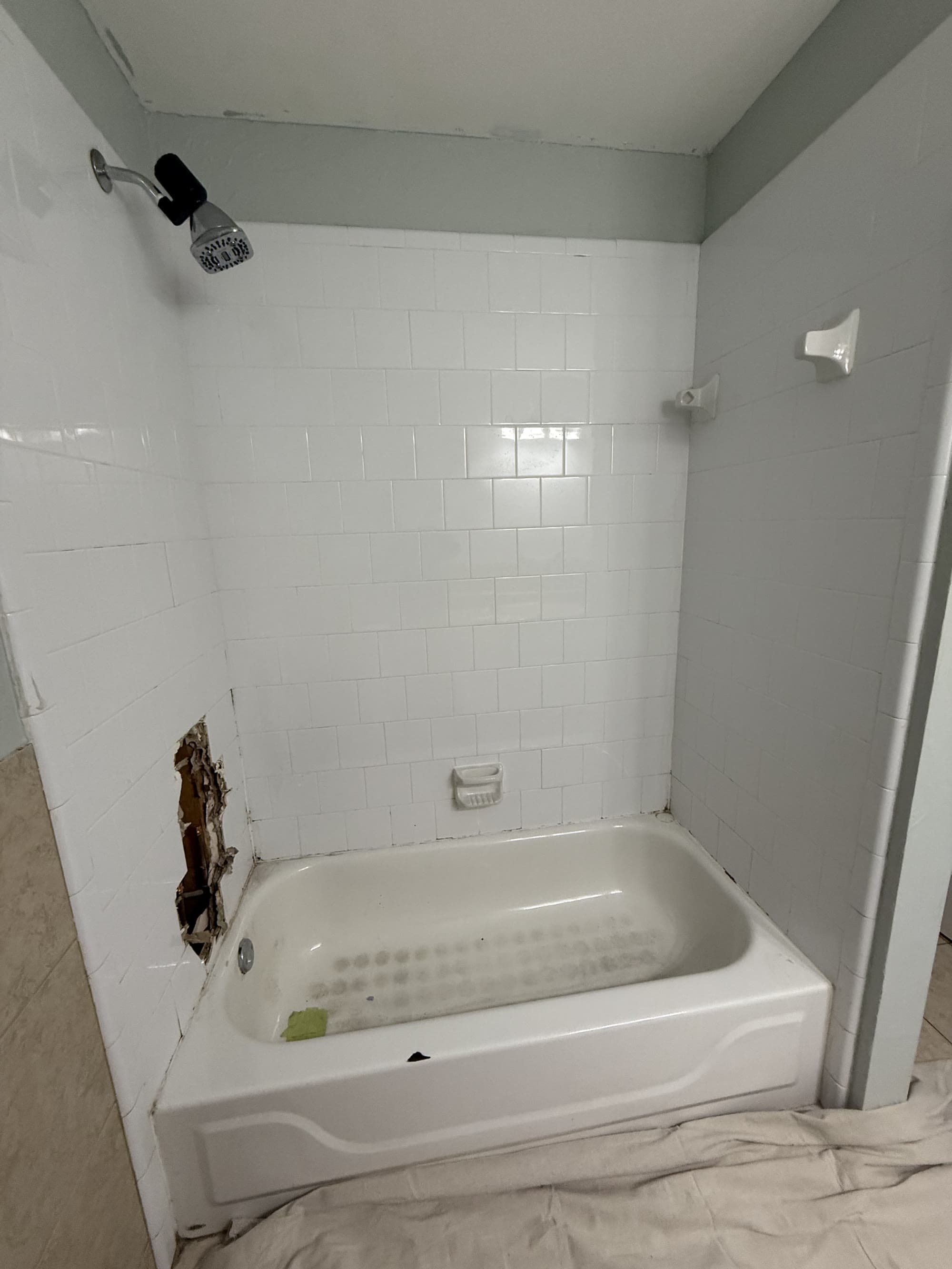 Original tub and subway tile shower surround with a section of wall removed before demo