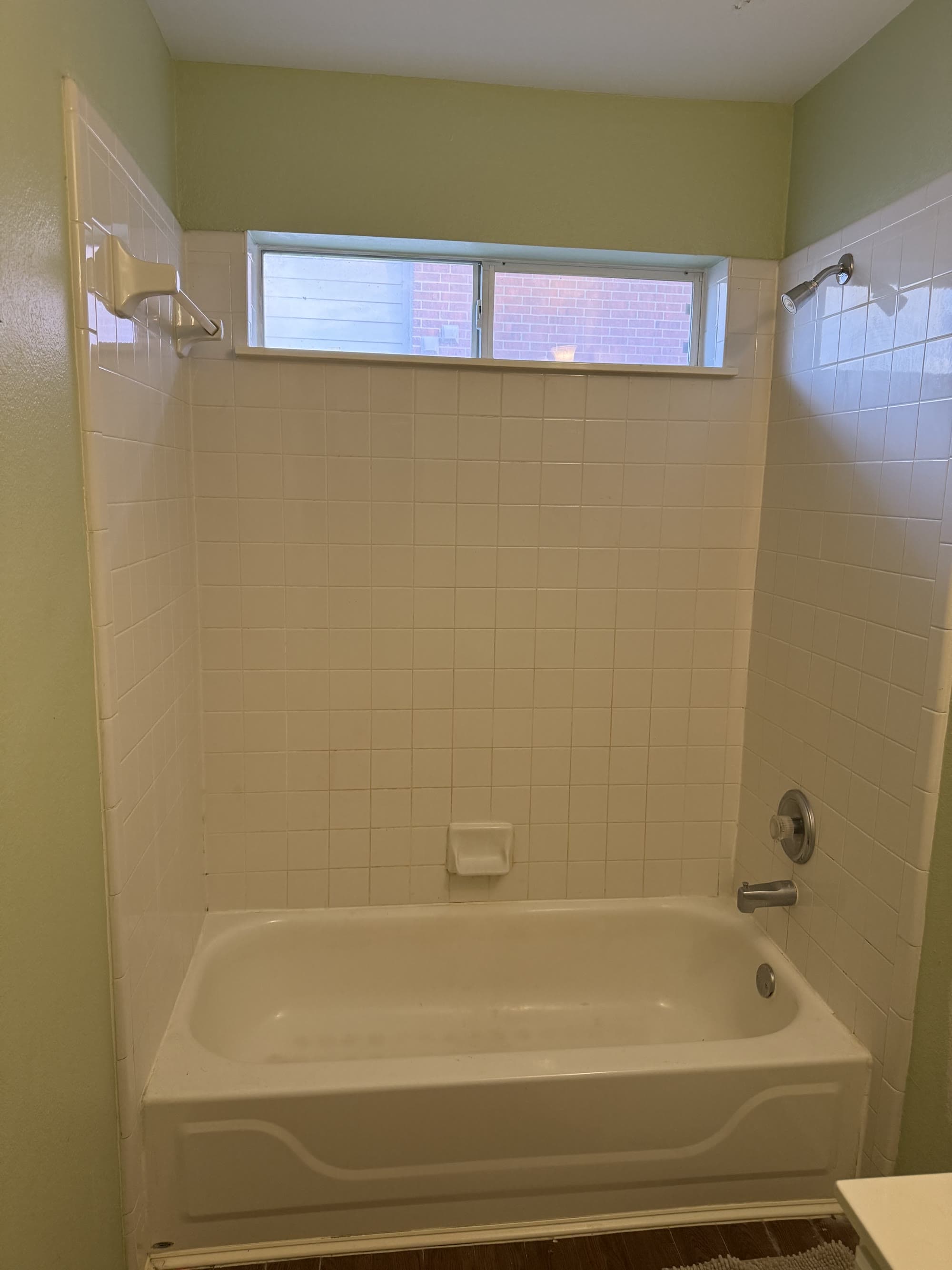 Dated bathroom with green walls and an old tub-shower combo before remodeling