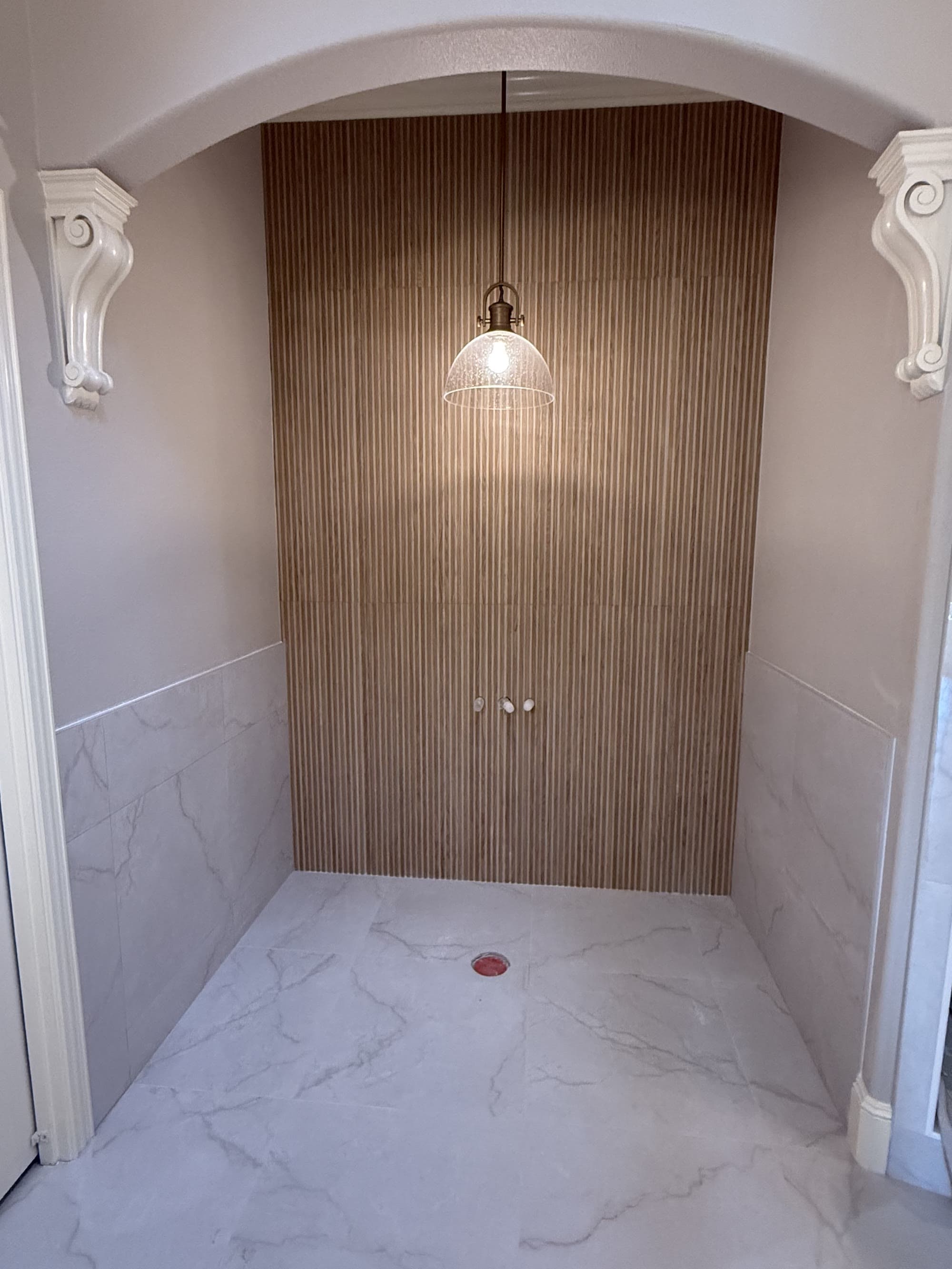 Walk-in shower alcove with marble-look tile and a wood slat accent wall under a pendant light