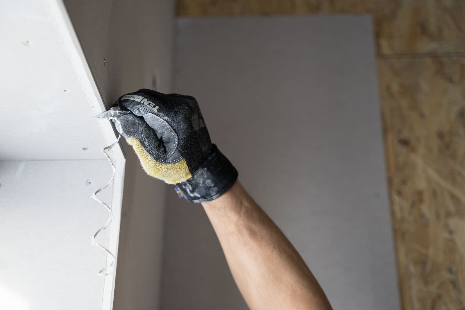 Gloved hand applying joint compound to a drywall patch with a taping knife